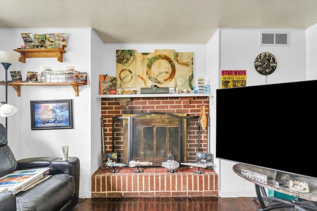 living area with a brick fireplace, wood finished floors, and visible vents