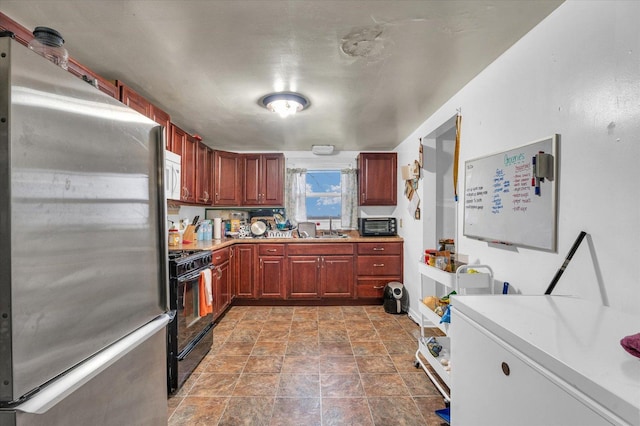 kitchen featuring white microwave, light countertops, freestanding refrigerator, gas stove, and a sink