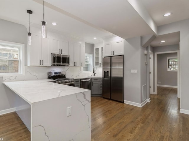 kitchen with kitchen peninsula, pendant lighting, white cabinetry, appliances with stainless steel finishes, and light stone counters