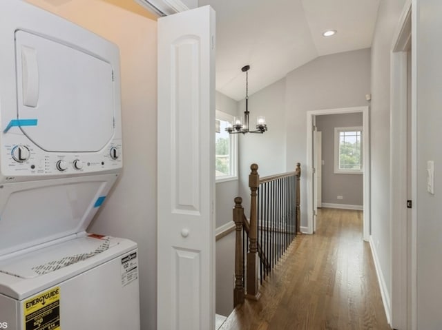 laundry room with stacked washer / drying machine, hardwood / wood-style flooring, and a chandelier