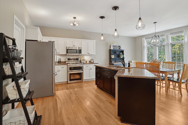 kitchen featuring decorative backsplash, appliances with stainless steel finishes, a kitchen island with sink, decorative light fixtures, and white cabinetry