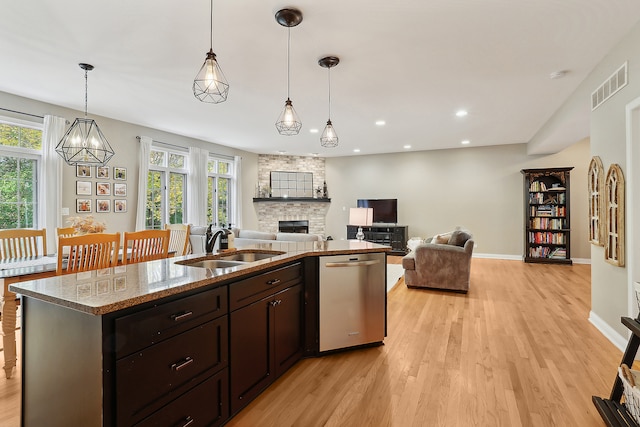 kitchen with sink, a stone fireplace, light stone counters, stainless steel dishwasher, and decorative light fixtures