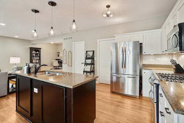 kitchen with sink, hanging light fixtures, stainless steel appliances, a kitchen island with sink, and white cabinets