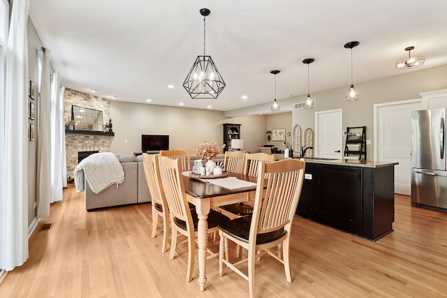 dining area with sink, a fireplace, an inviting chandelier, and light hardwood / wood-style flooring