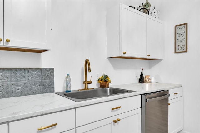 kitchen with stainless steel dishwasher, light stone counters, white cabinets, and sink