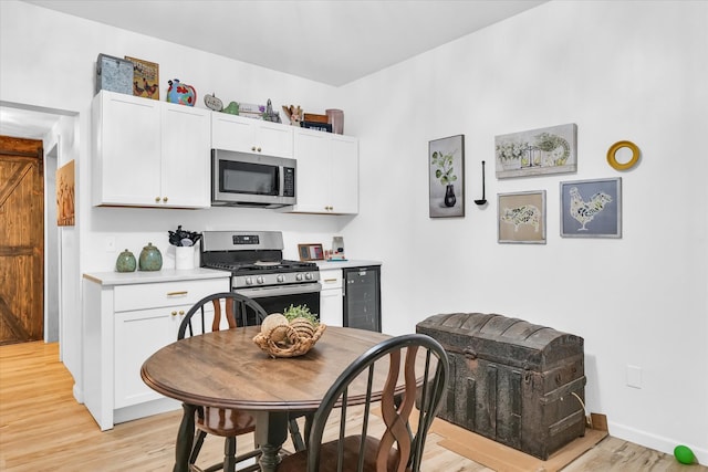 kitchen with white cabinets, appliances with stainless steel finishes, wine cooler, and light hardwood / wood-style flooring