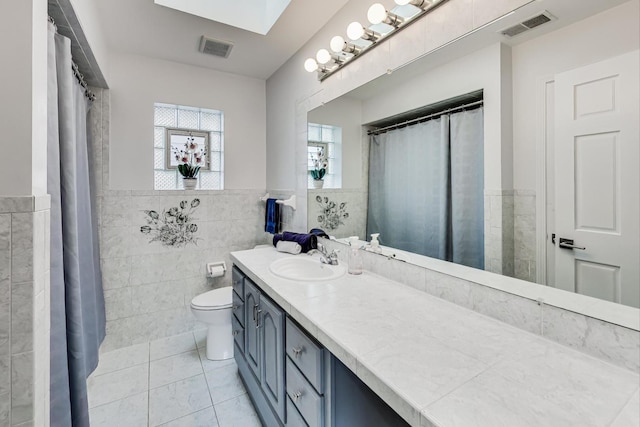 bathroom with a skylight, tile patterned floors, vanity, tile walls, and toilet