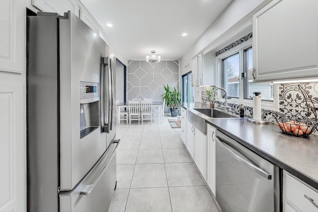 kitchen with white cabinetry, sink, decorative backsplash, light tile patterned floors, and appliances with stainless steel finishes