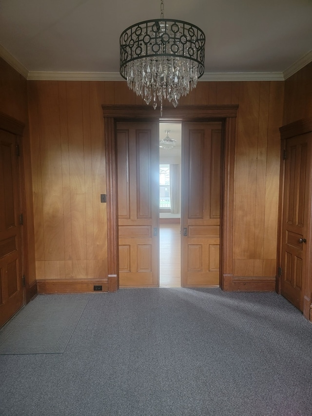 dining space with carpet flooring, wood walls, ornamental molding, and an inviting chandelier