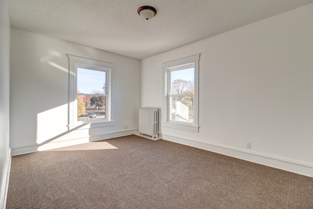 carpeted spare room with a wealth of natural light, a textured ceiling, and radiator heating unit