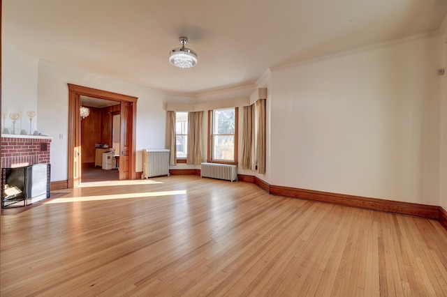 unfurnished living room featuring radiator, light wood-type flooring, ornamental molding, and a brick fireplace