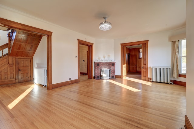 unfurnished living room with light wood-type flooring, radiator heating unit, ornamental molding, and a brick fireplace