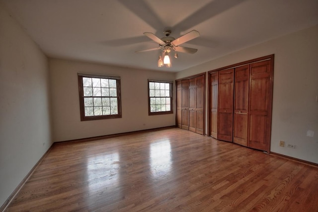 unfurnished bedroom with light hardwood / wood-style floors, ceiling fan, and multiple closets