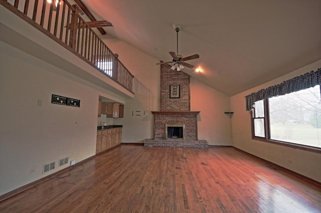 unfurnished living room with ceiling fan, sink, high vaulted ceiling, a fireplace, and hardwood / wood-style floors