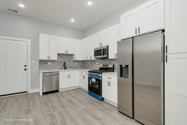 kitchen featuring appliances with stainless steel finishes, sink, light wood-type flooring, backsplash, and white cabinetry