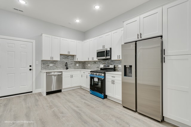 kitchen with stainless steel appliances, sink, white cabinets, light hardwood / wood-style floors, and tasteful backsplash