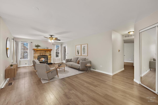 living room featuring ceiling fan, a stone fireplace, and light hardwood / wood-style flooring