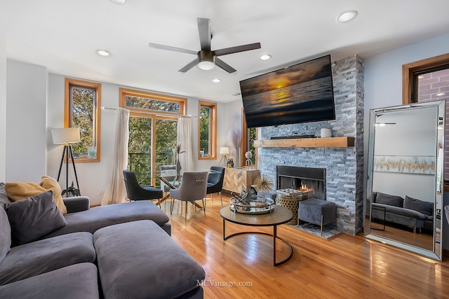 living room featuring a stone fireplace, wood-type flooring, and ceiling fan