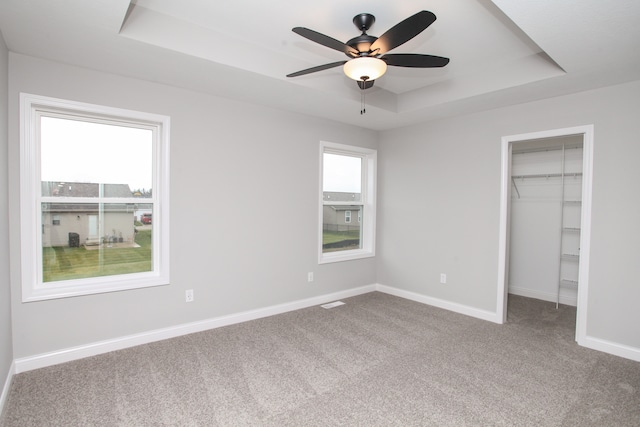 unfurnished bedroom with ceiling fan, carpet flooring, a closet, and a tray ceiling