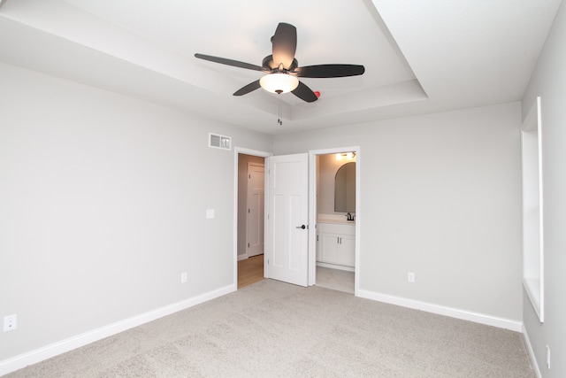 unfurnished bedroom featuring ensuite bathroom, light colored carpet, ceiling fan, and a tray ceiling