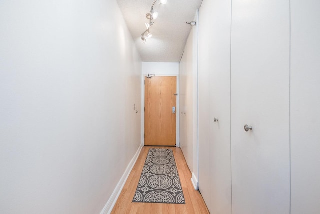 hallway with track lighting, light hardwood / wood-style floors, and a textured ceiling