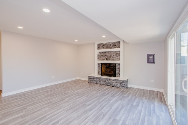 unfurnished living room featuring light wood-type flooring and a stone fireplace