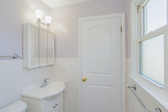 bathroom featuring vanity, toilet, a wealth of natural light, and tile walls