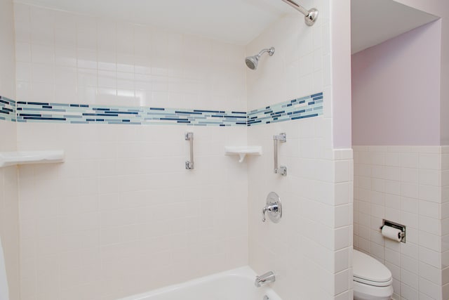 bathroom with tiled shower / bath, toilet, and tile walls