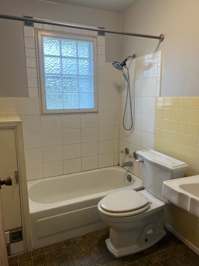 bathroom featuring tile patterned flooring, tiled shower / bath combo, toilet, and tile walls