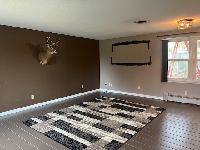 spare room with baseboard heating and dark hardwood / wood-style floors