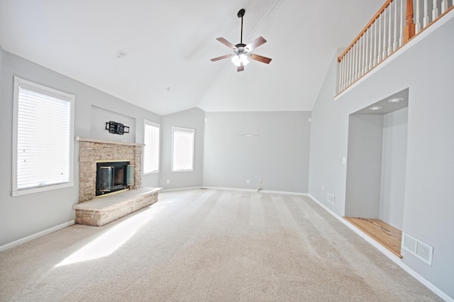 unfurnished living room with light colored carpet, a stone fireplace, plenty of natural light, and ceiling fan