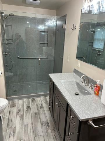 bathroom featuring toilet, wood finished floors, vanity, and a stall shower