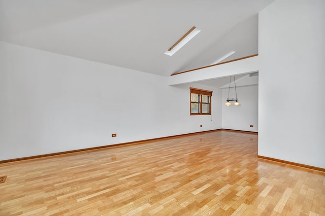 empty room featuring vaulted ceiling with skylight, a notable chandelier, and light hardwood / wood-style flooring