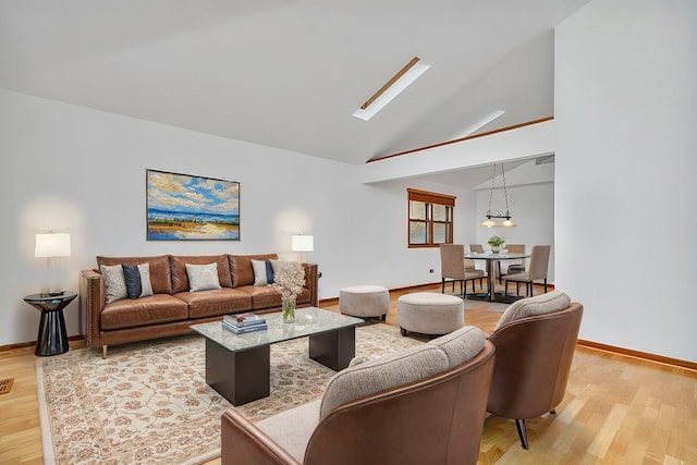 living room with light wood-type flooring, a skylight, and high vaulted ceiling