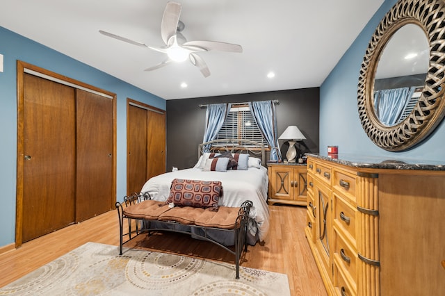 bedroom with light hardwood / wood-style floors, ceiling fan, and two closets