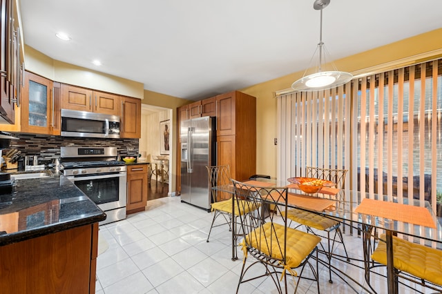 kitchen with tasteful backsplash, stainless steel appliances, dark stone counters, decorative light fixtures, and light tile patterned floors