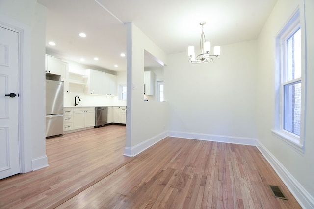 unfurnished dining area with a chandelier, sink, a wealth of natural light, and light hardwood / wood-style flooring