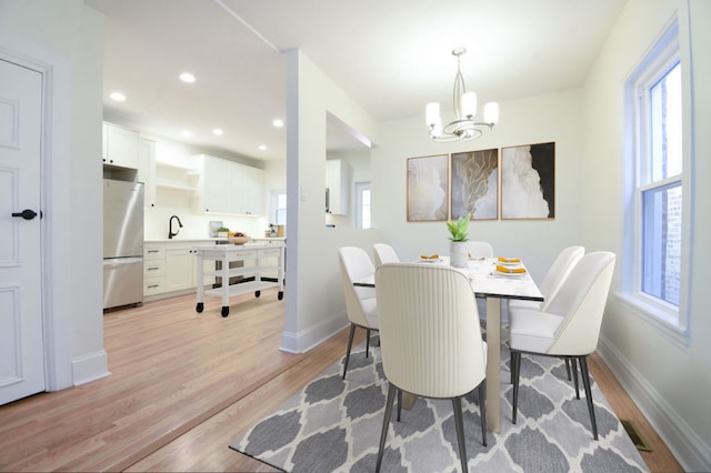 dining room with a notable chandelier, sink, and light hardwood / wood-style flooring