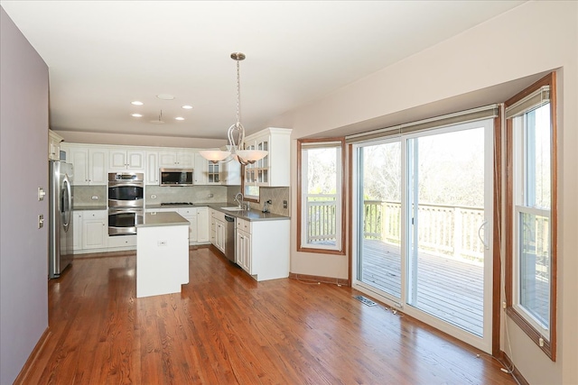 kitchen with white cabinetry, hanging light fixtures, dark wood-type flooring, stainless steel appliances, and a kitchen island