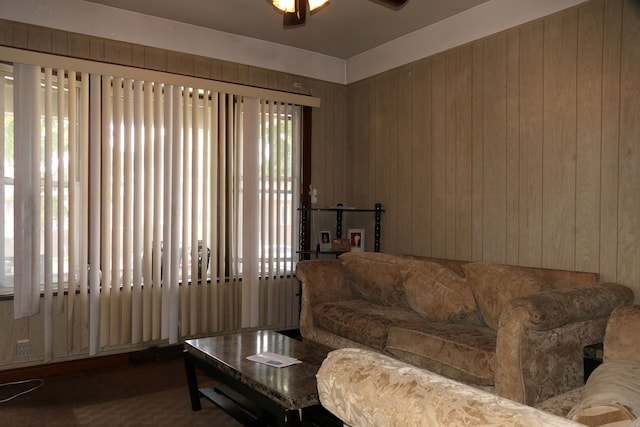 carpeted living room featuring wood walls and ceiling fan