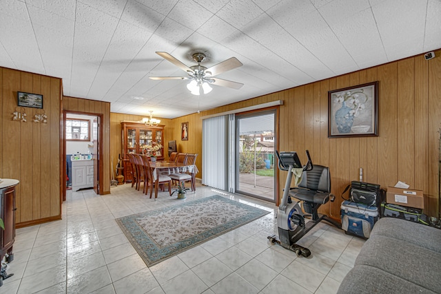 tiled living room with ceiling fan with notable chandelier and wooden walls