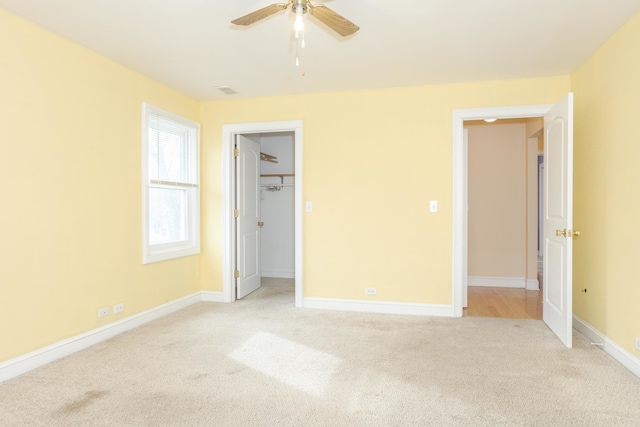 unfurnished bedroom featuring a closet, light colored carpet, a spacious closet, and ceiling fan