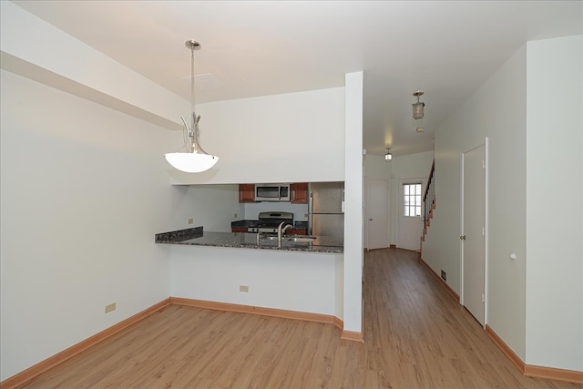 kitchen with kitchen peninsula, appliances with stainless steel finishes, decorative light fixtures, and light hardwood / wood-style flooring