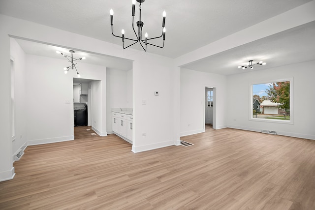 unfurnished dining area featuring light wood-type flooring, a textured ceiling, and a chandelier