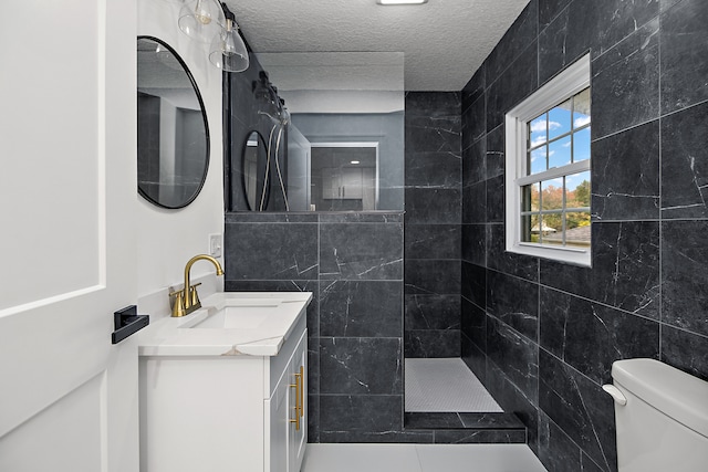 bathroom featuring tile walls, a tile shower, vanity, a textured ceiling, and toilet