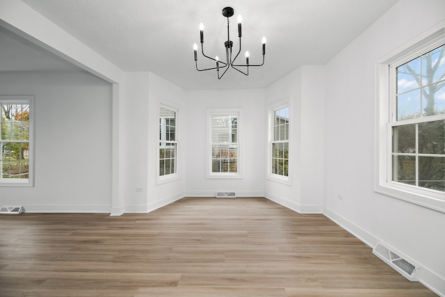 unfurnished dining area featuring a textured ceiling, light wood-type flooring, and a chandelier