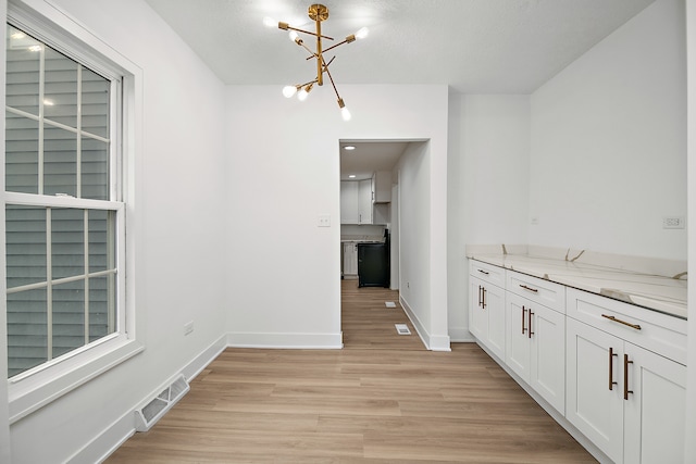 kitchen with an inviting chandelier, a textured ceiling, light stone countertops, white cabinetry, and light hardwood / wood-style flooring