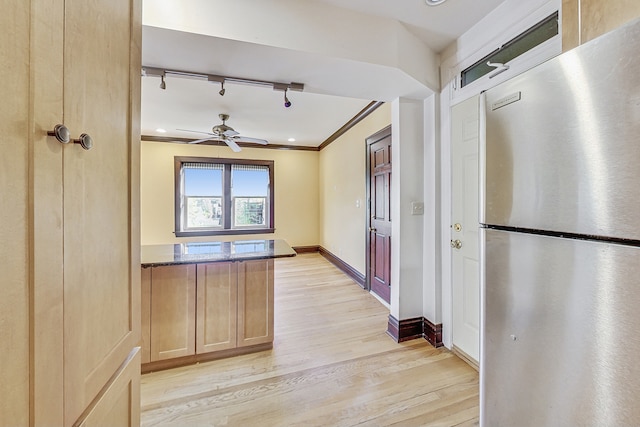 kitchen with light hardwood / wood-style floors, ceiling fan, crown molding, stainless steel refrigerator, and dark stone countertops