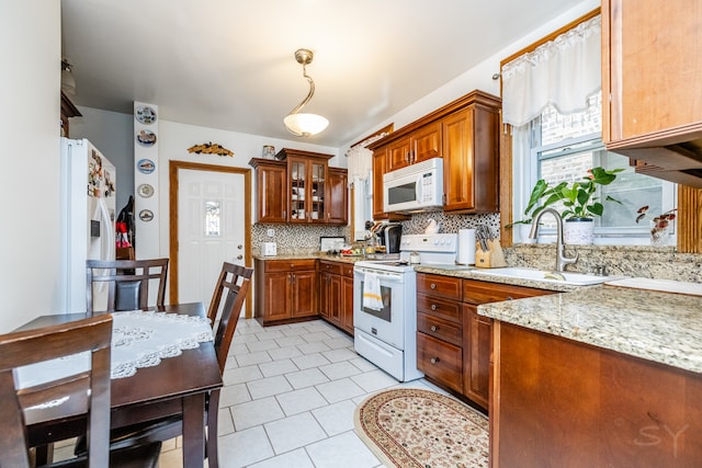 kitchen featuring hanging light fixtures, backsplash, sink, light stone countertops, and white appliances