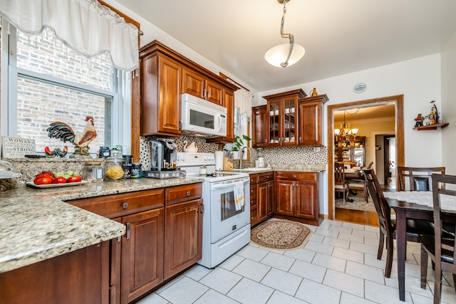 kitchen with hanging light fixtures, light stone countertops, a notable chandelier, white appliances, and tasteful backsplash